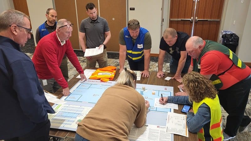 School staff, law enforcement, fire, and EMS gather around a Counterstrike Reunification environment map, working the response and reunification plan together